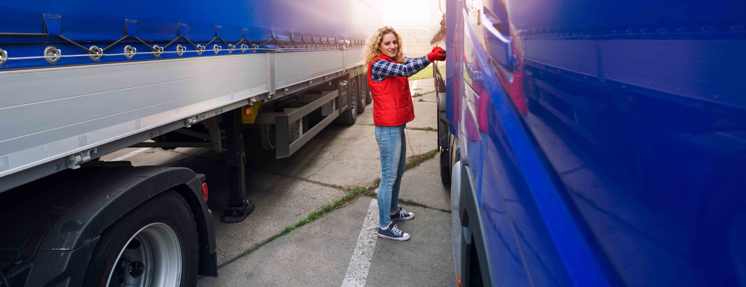 Female trucker removing canvas tarpaulin to prepare truck for unloading.